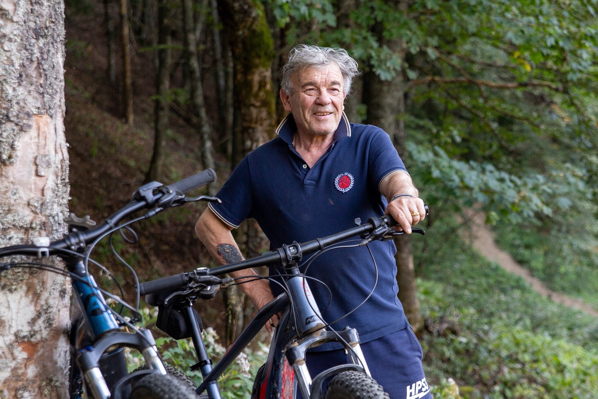 Un uomo sorridente con due biciclette nel bosco